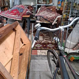 Verzameling tweedehands meubels en huishoudartikelen in een kringloopwinkel, waaronder een fiets, houten kastje, tapijten en 