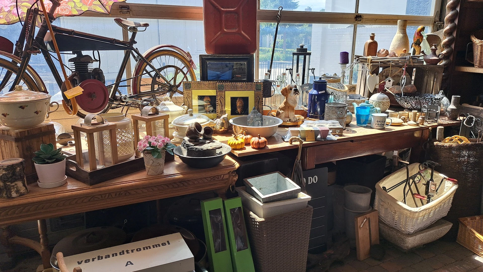 Houten tafel vol huishoudspullen, servies, decoratieartikelen en vintage items in een kringloopwinkel