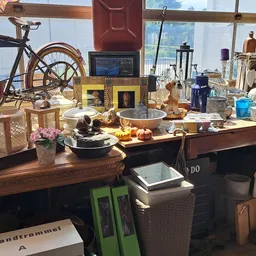 Houten tafel vol huishoudspullen, servies, decoratieartikelen en vintage items in een kringloopwinkel