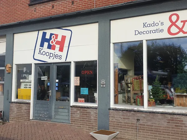 Winkelfront met H&H Koopjes-logo en Krado's Decoratie & naambord, bakstenen gevel met glazen deuren en ramen.