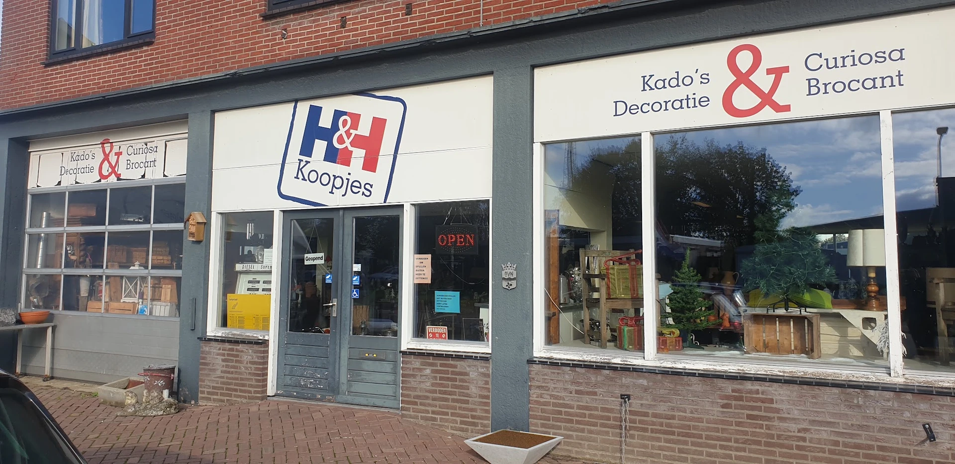 Winkelfront met H&H Koopjes-logo en Krado's Decoratie & naambord, bakstenen gevel met glazen deuren en ramen.