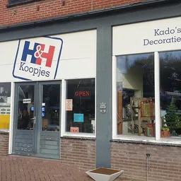 Winkelfront met H&H Koopjes-logo en Krado's Decoratie & naambord, bakstenen gevel met glazen deuren en ramen.