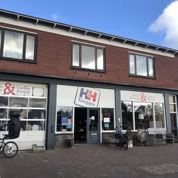 Voorgevel van kringloopwinkel met bruine bakstenen, grote ramen en donkerblauwe deuren, fietsen ervoor