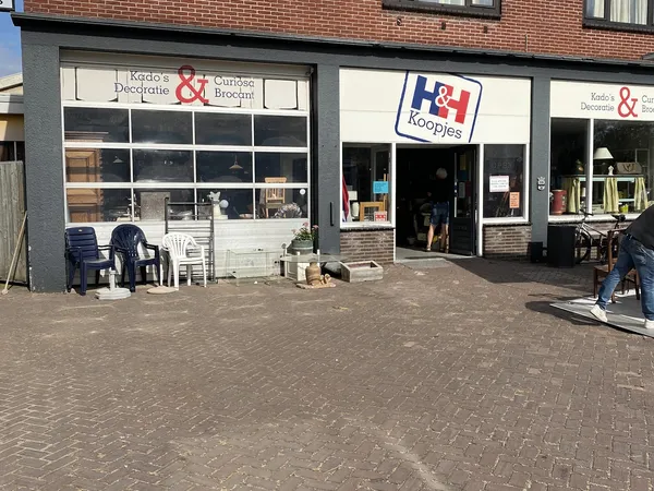 Gevel van kringloopwinkel met etalageruiten, ingang en uitstallingen op het terras