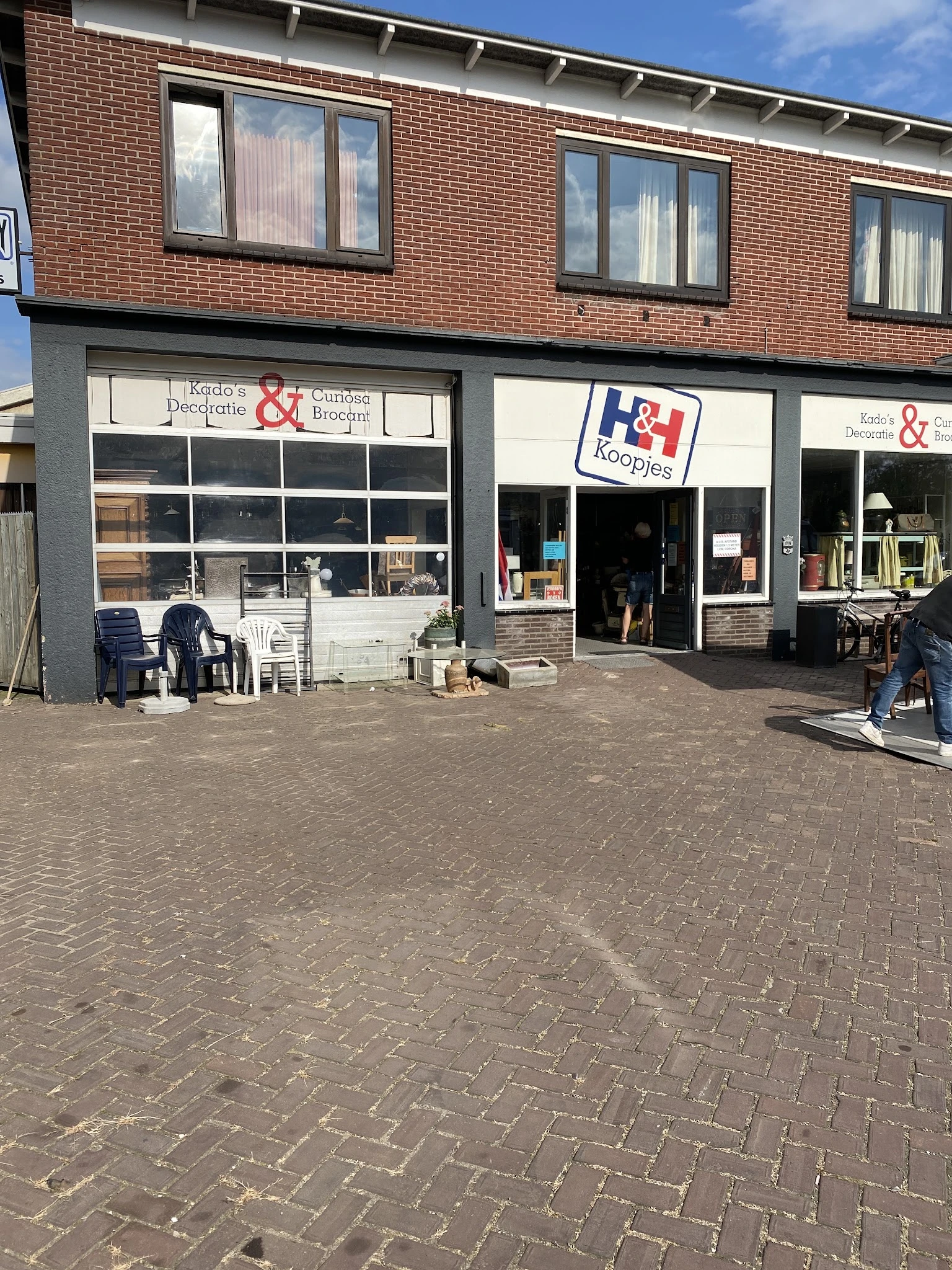 Gevel van kringloopwinkel met etalageruiten, ingang en uitstallingen op het terras