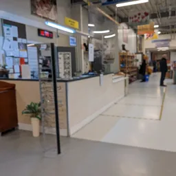 Binnenaanzicht van kringloopwinkel met balie, stellingen met spullen en klanten in het achtergrond