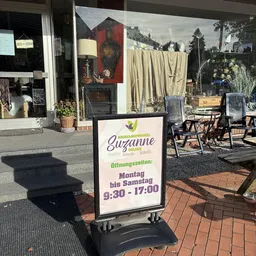 Openingstijdenbord van kringloopwinkel Suzanne met winkelvoorgevel op achtergrond