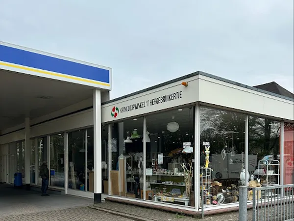 Winkelgevel van kringloopwinkel 't Hergebruikertje met etalage vol spullen, witte afzetting en blauwe afdak links