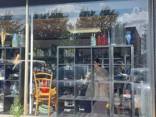 Binnenaanzicht van kringloopwinkel met glazen scheidingswanden, stellingen vol spullen en een medewerker achter de toonbank