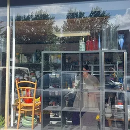 Binnenaanzicht van kringloopwinkel met glazen scheidingswanden, stellingen vol spullen en een medewerker achter de toonbank