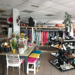 Winkelvloer met kledingrekken, schoenen op display, bloemen en stoelen in een kringloopwinkel