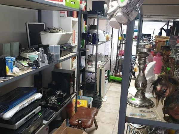 Binnenaanzicht van kringloopwinkel met stellingen, werkbank en diverse tweedehandsartikelen