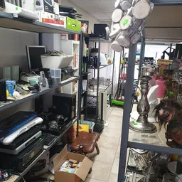 Binnenaanzicht van kringloopwinkel met stellingen, werkbank en diverse tweedehandsartikelen