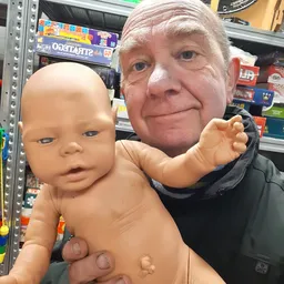 Een man houdt een naakte babypop vast in een kringloopwinkel