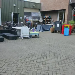 Voorkant kringloopwinkel met terras, fietsen, stellingen en spullen buiten uitgestald