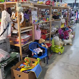 Winkelvloer met houten stellingen vol speelgoed, knuffels en kinderspullen in een kringloopwinkel