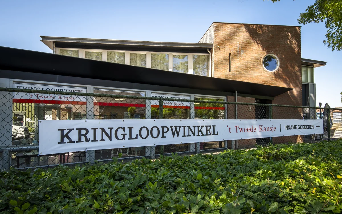 Voorgevel van kringloopwinkel met bakstenen bovenbouw en donkere ondergrond, winkelnaam duidelijk zichtbaar op bord