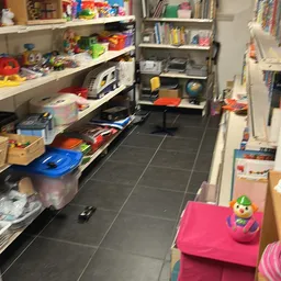 Speelgoedwinkel met speelgoed op stellingen en op de vloer, zwarte tegels zichtbaar
