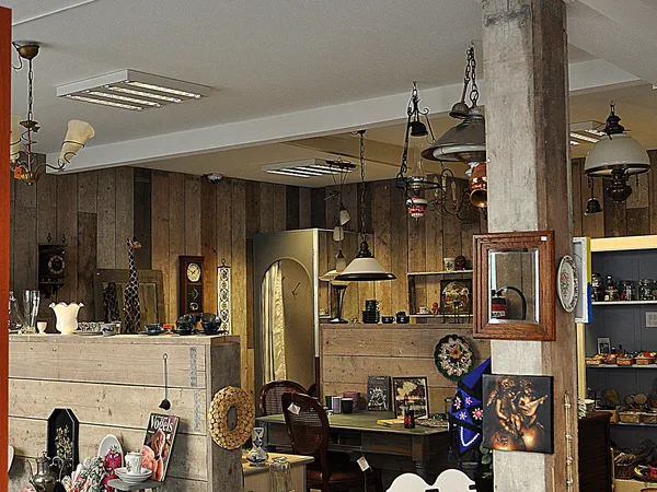 Interieur van kringloopwinkel met houten wanden, diverse hangende lampen, kasten met spullen en decoratieve voorwerpen