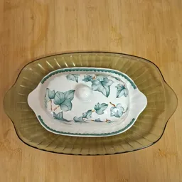 Twee gestapelde decoratieve schalen met bloemmotief, de onderste groen en de bovenste met blauwe bloemen en witte grepen