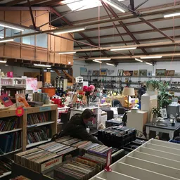 Overzicht van kringloopwinkel met boeken, vinyl, meubels en huishoudspullen op verschillende niveaus