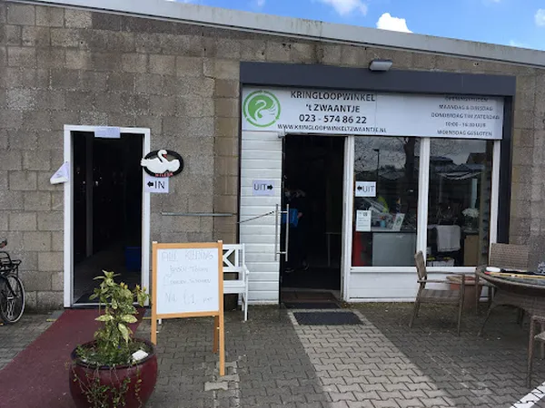 Gevel van kringloopwinkel 't Zwaantje met witte en zwarte deuren, etalageruiten en informatieborden