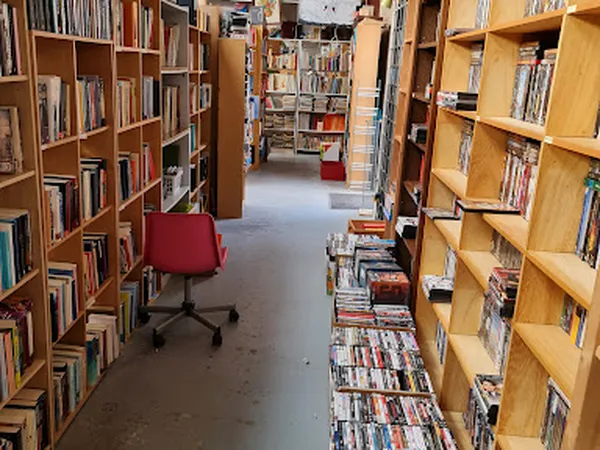 Winkelinterieur met houten boekenkasten vol boeken en dvd's, rood bureaustoel, grijs linoleum vloer