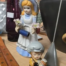 Twee porseleinpoppen met blauwe accenten en bloemen, één popmotief op de voet van de andere