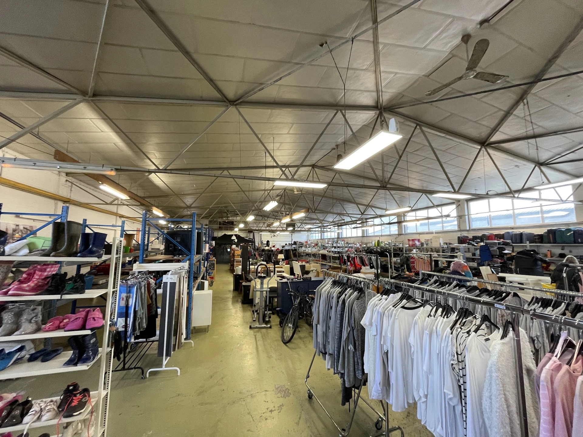 Ruime winkelhal met kledingrekken vol tweedehands kleding, industrieel plafond met verlichting