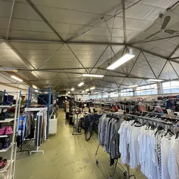 Ruime winkelhal met kledingrekken vol tweedehands kleding, industrieel plafond met verlichting