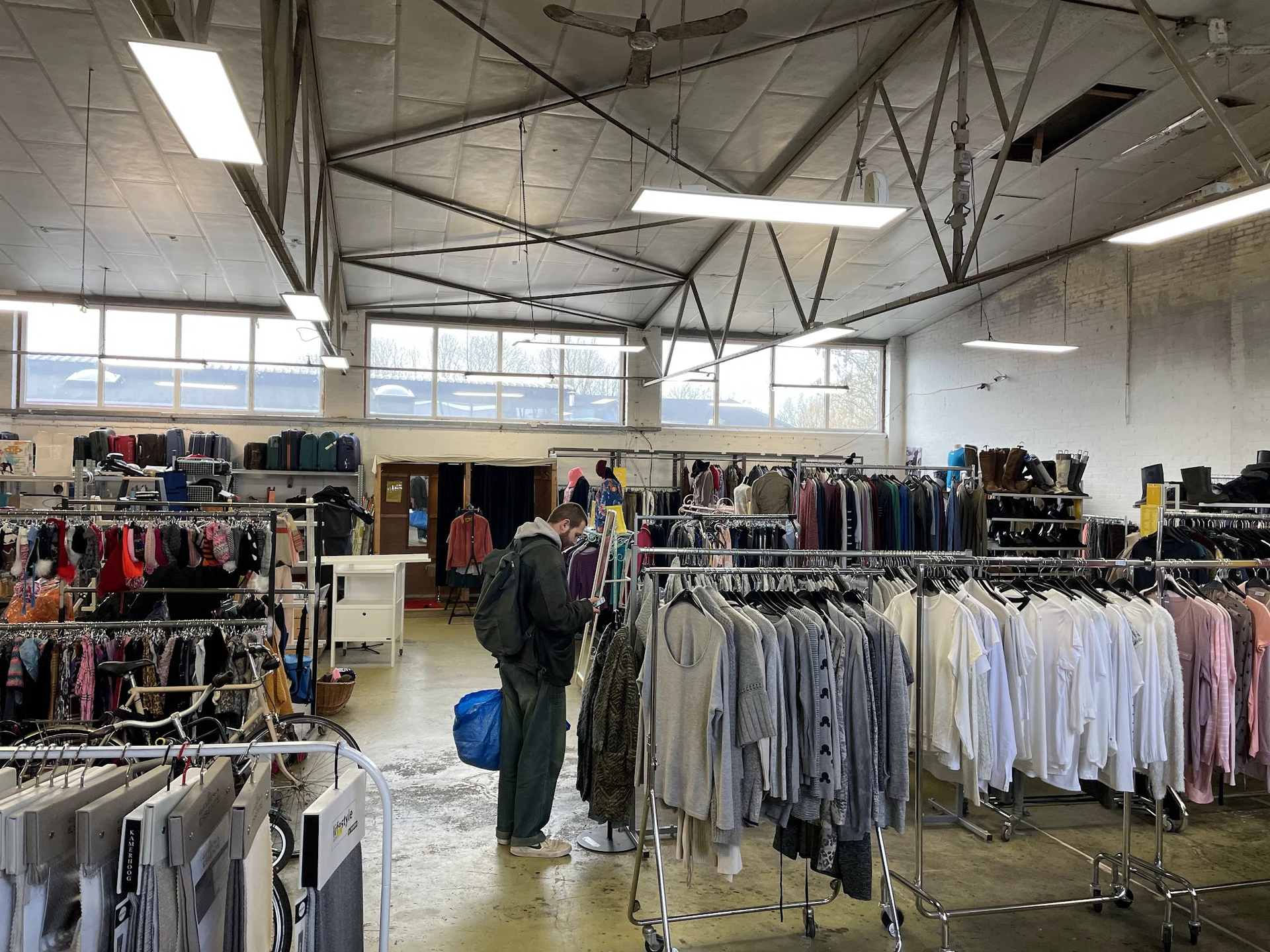 Overzicht van de winkelvloer met meerdere kledingrekken vol tweedehands kleding in verschillende kleuren, onder een hoog plaf