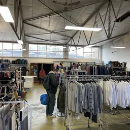 Overzicht van de winkelvloer met meerdere kledingrekken vol tweedehands kleding in verschillende kleuren, onder een hoog plaf