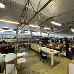 Ruim magazijn- of winkelvloer met verschillende afdelingen, tafels met spullen, rekken met kleding en diverse tweedehandsarti