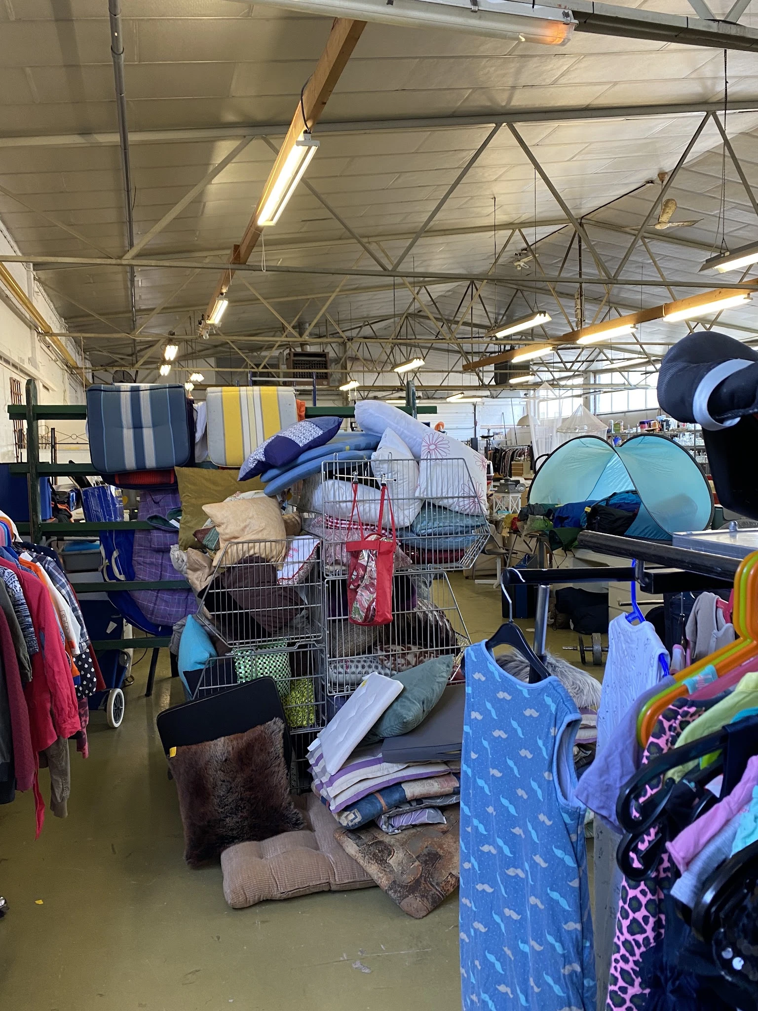 Winkelvloer met stellingen vol tweedehands spullen: kleding, tenten, kampeerstoelen en overig huishoudgoed