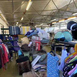 Winkelvloer met stellingen vol tweedehands spullen: kleding, tenten, kampeerstoelen en overig huishoudgoed