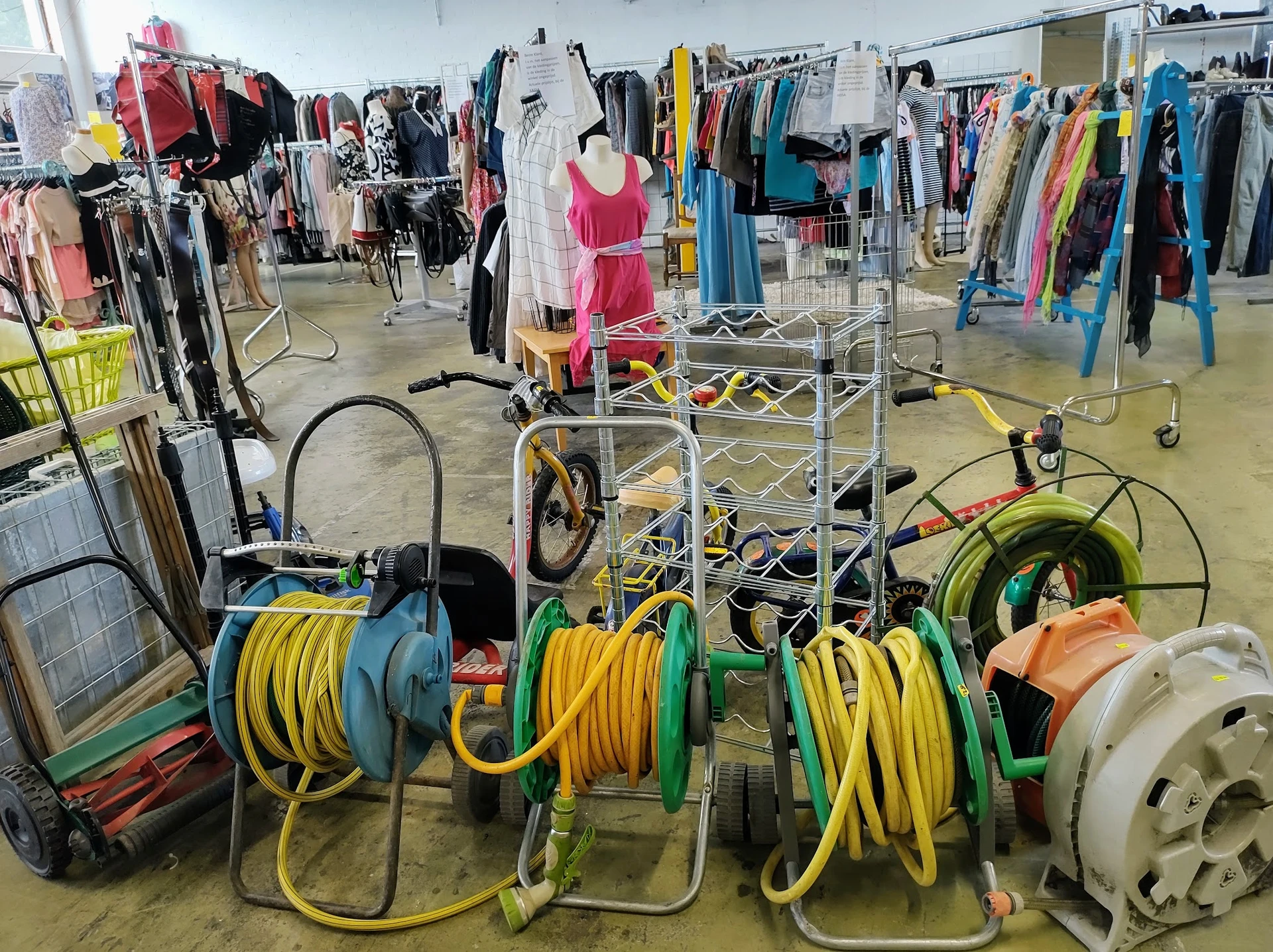 Winkelvloer met sieraden, elektrische kabels op krullen en kledingrekken met tweedehands kleding op de achtergrond
