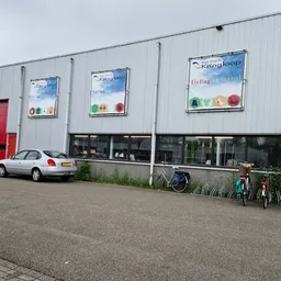 Wit golfplaten pand met rode deur, winkelramen en uitgestalde fietsen op het parkeerterrein