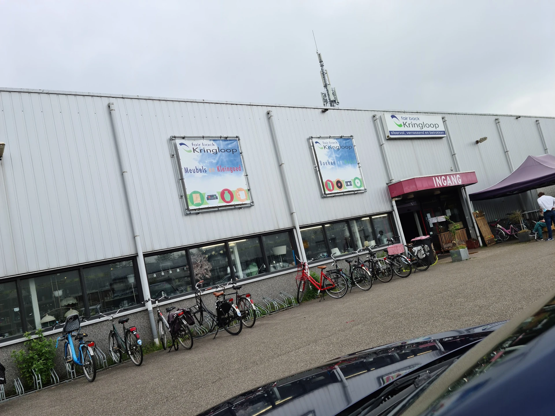 Witte gevel van kringloopwinkel met ramen, deuren en fietsen geparkeerd ervoor