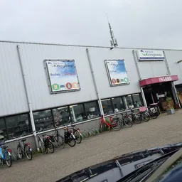 Witte gevel van kringloopwinkel met ramen, deuren en fietsen geparkeerd ervoor