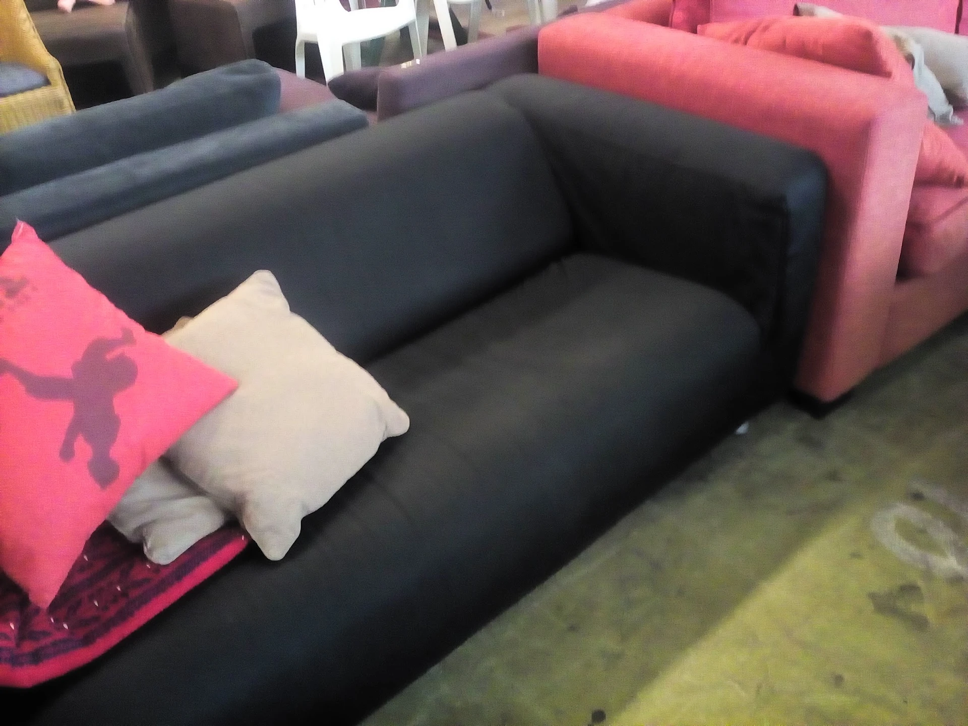 Donkerblauwe tweedehands bank of sofa met witte en roze kussens in een kringloopwinkel