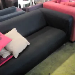 Donkerblauwe tweedehands bank of sofa met witte en roze kussens in een kringloopwinkel