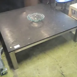 Zwarte vierkante salontafel met glaswerk op het blad, op een betonnen winkelvloer