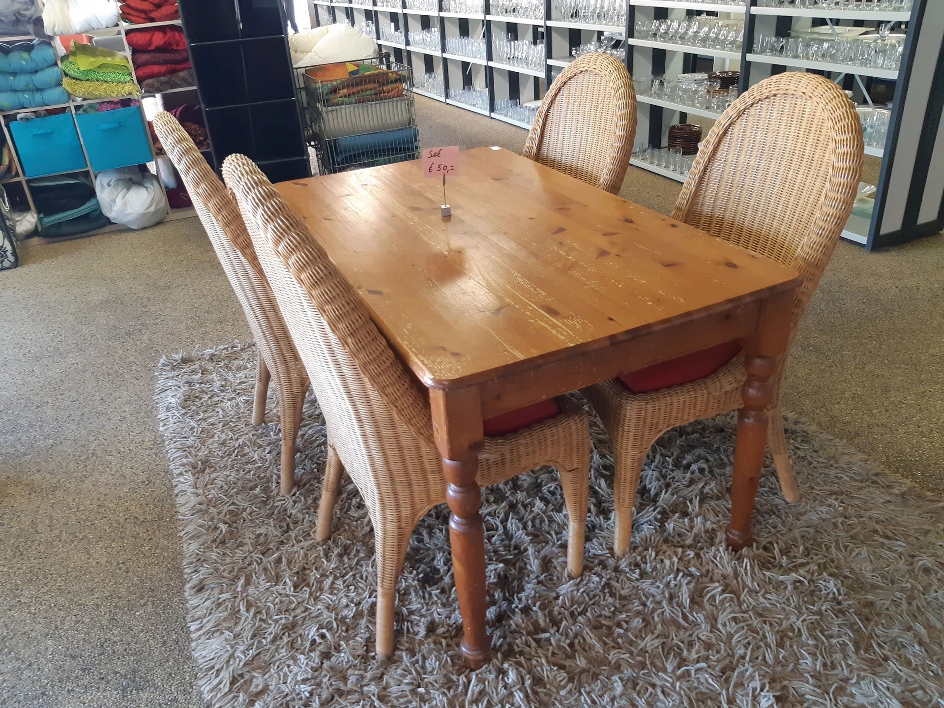 Houten eettafel met vier rieten stoelen op een grijze vloerkleed in een kringloopwinkel
