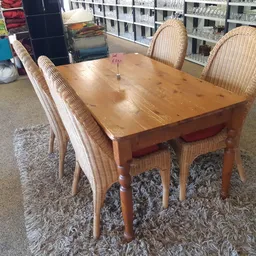 Houten eettafel met vier rieten stoelen op een grijze vloerkleed in een kringloopwinkel