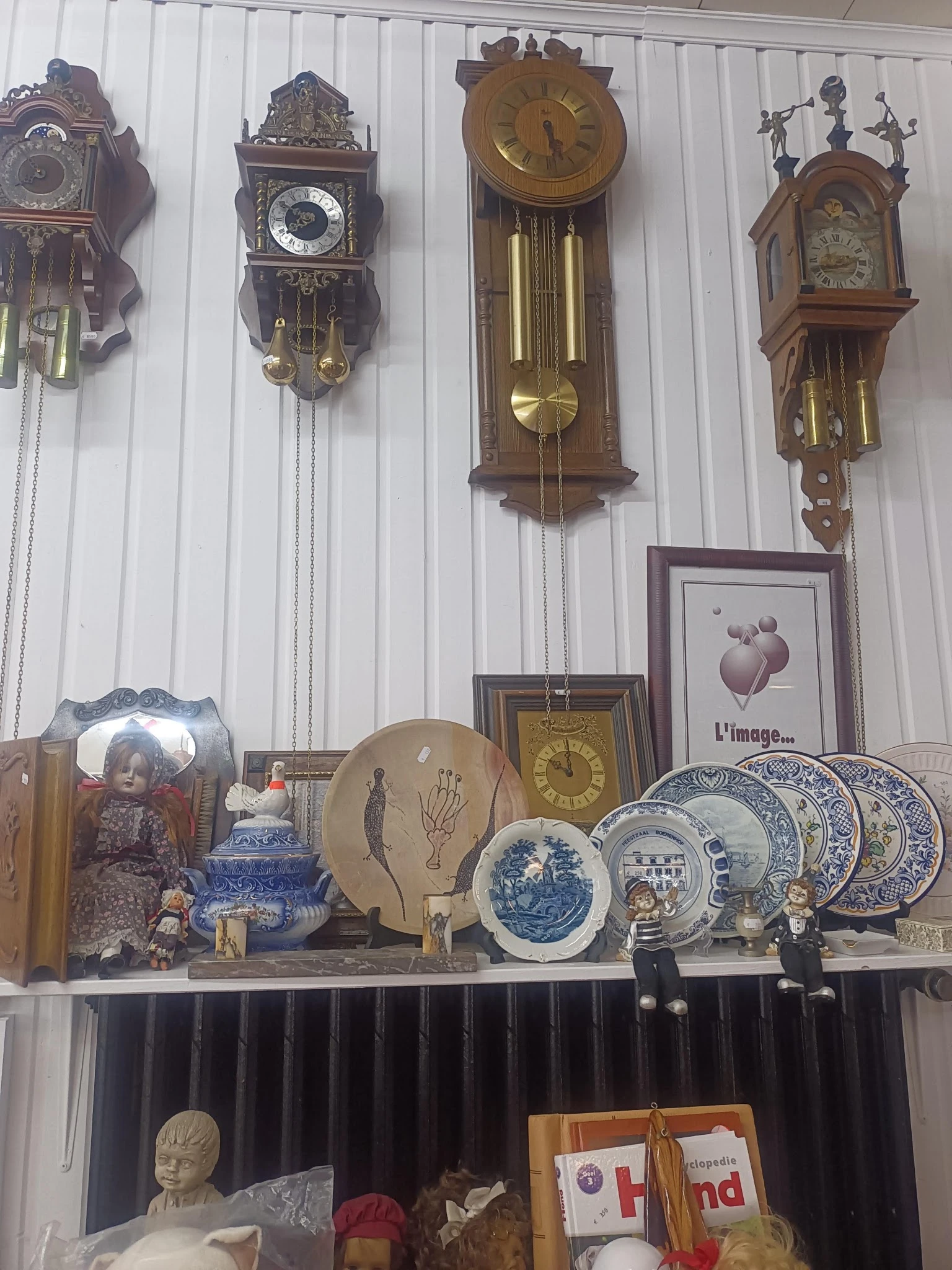 Uitgestalde decoratieve artikelen: wandklokken, borden, servies en andere vintage huishoudartikelen op een plank