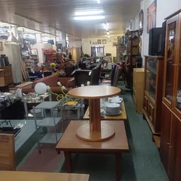 Winkelvloer van kringloopwinkel met ronde tafel, serviesgoed, meubels en verschillende afdelingen op achtergrond