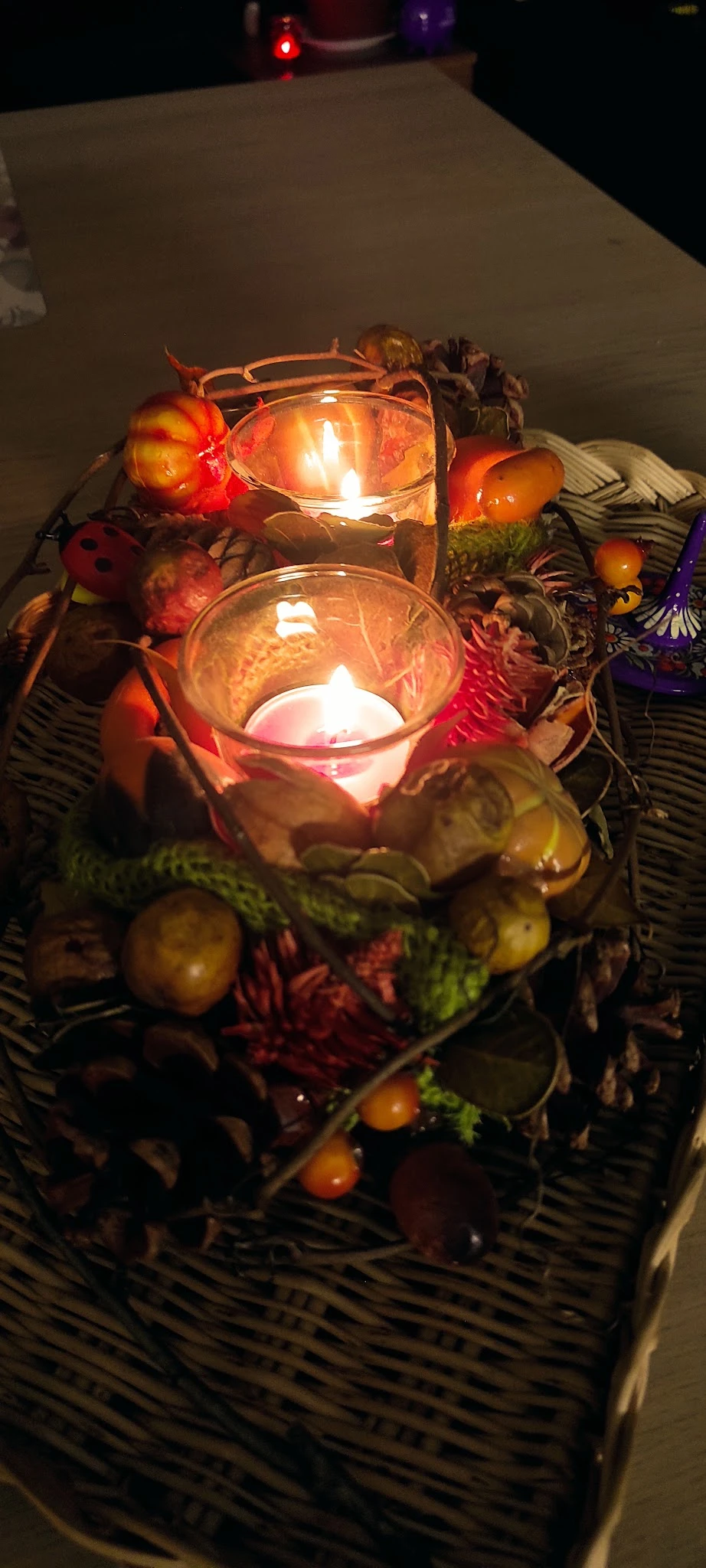 Glazen kaarshouder met brandende kaars omgeven door decoratieve herfstbladeren en andere ornamenten