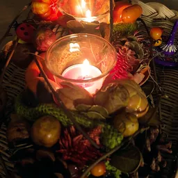 Glazen kaarshouder met brandende kaars omgeven door decoratieve herfstbladeren en andere ornamenten
