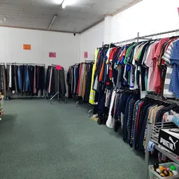 Kringloopwinkel met kledingrekken, stellingen en diverse tweedehands artikelen op groene vloer