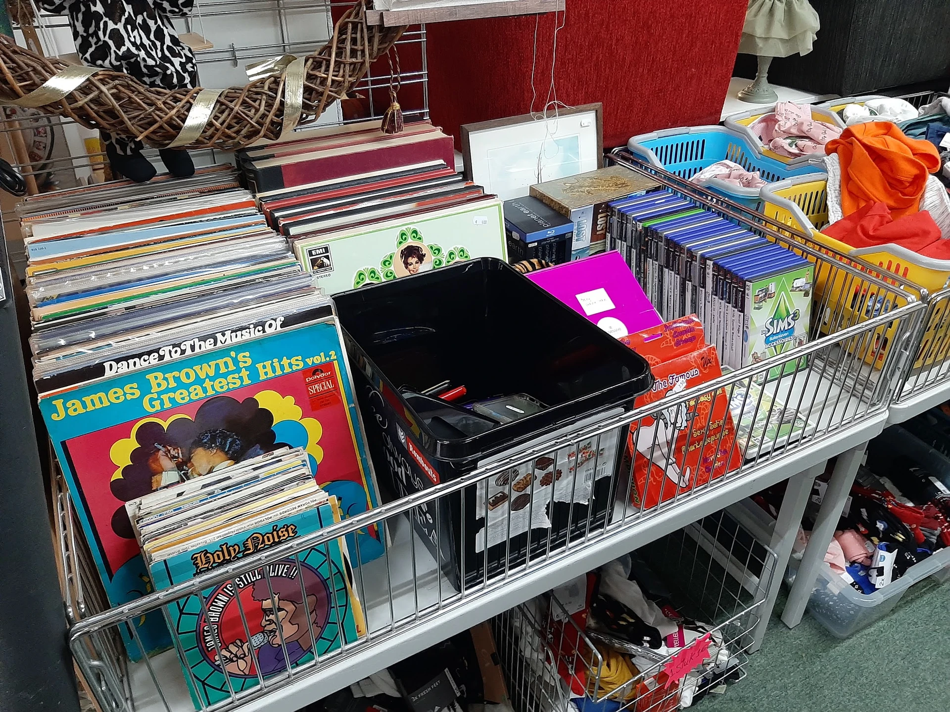 Uitgestalde tweedehands spullen op tafels: vinyl records, boeken, dvd's, speelgoed en kleding in bakken